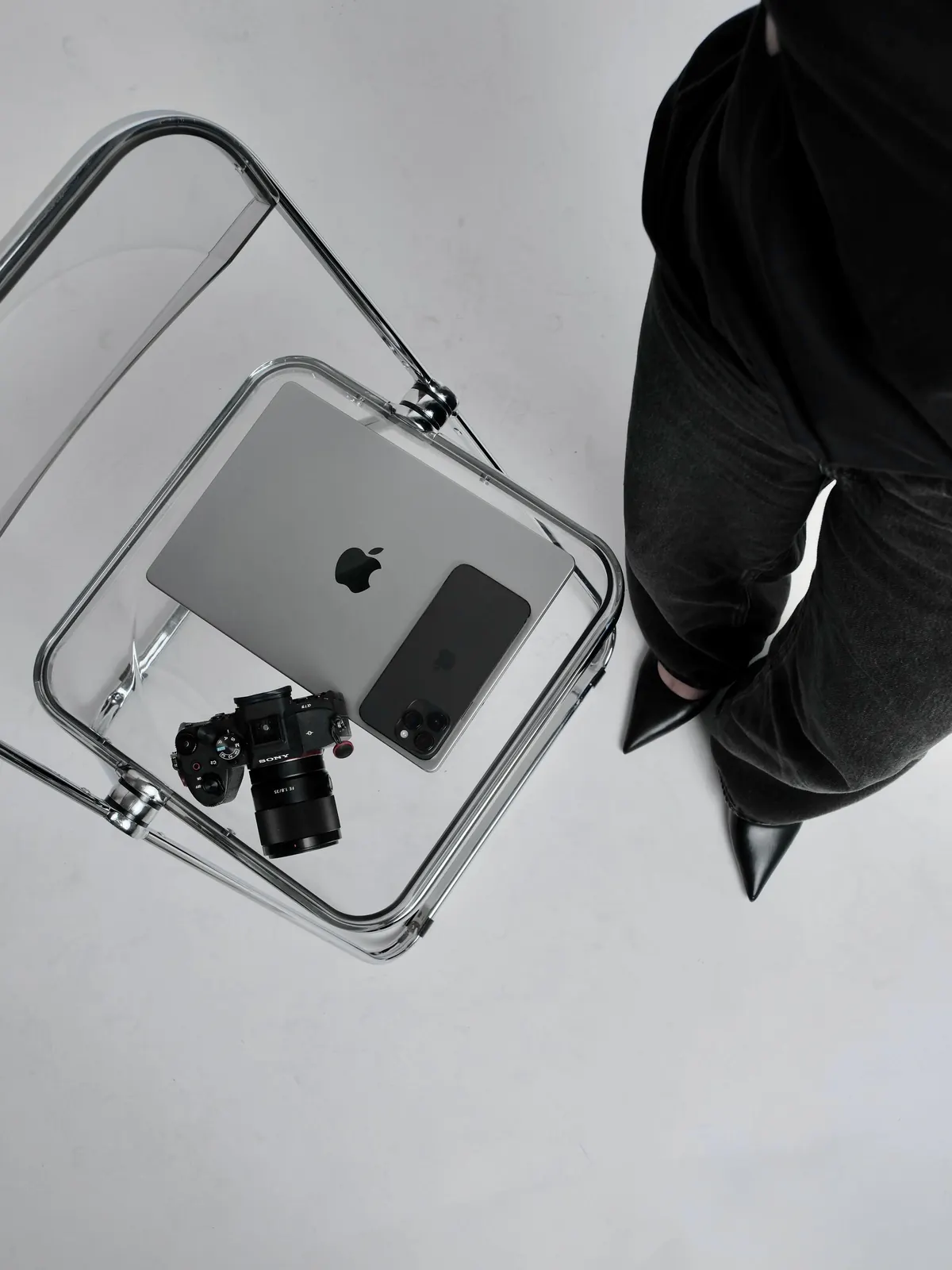 A camera, a laptop and a phone resting on a clear acrylic chair.
